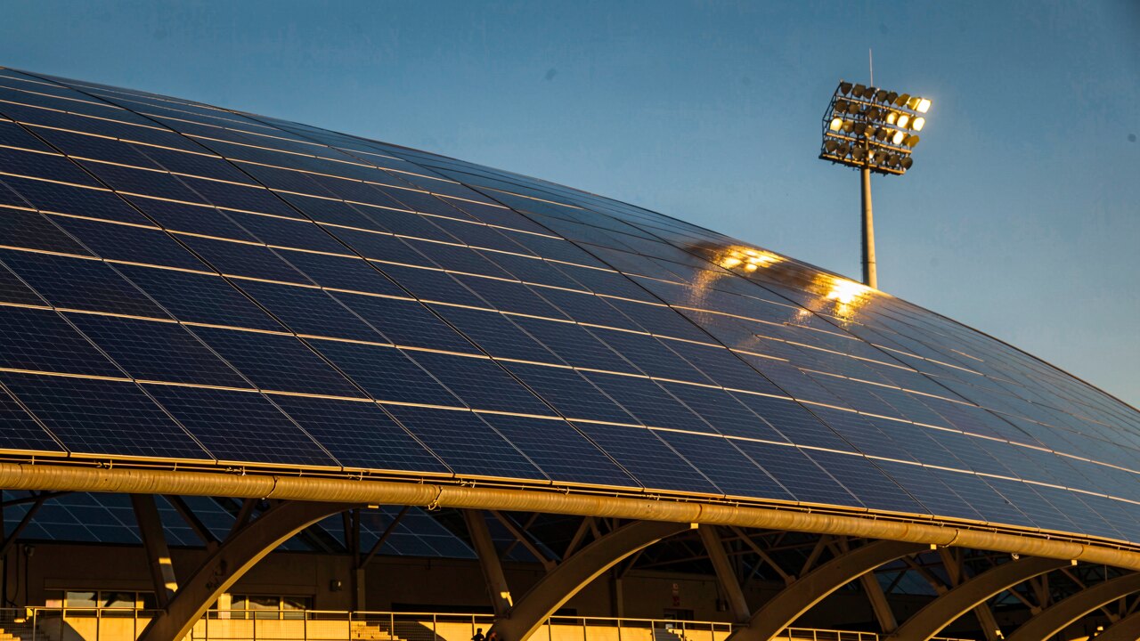 Nahaufnahme eines Stadiondachs voller blauer Solarmodule in der Abendsonne — Illustration